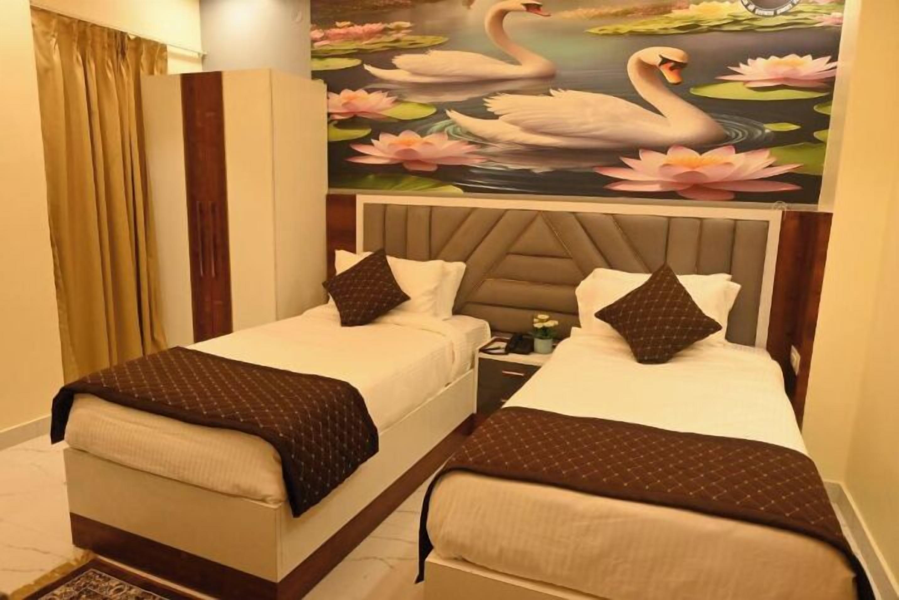 A hotel room with two beds, a headboard with a floral mural, and a bedside table with a lamp.