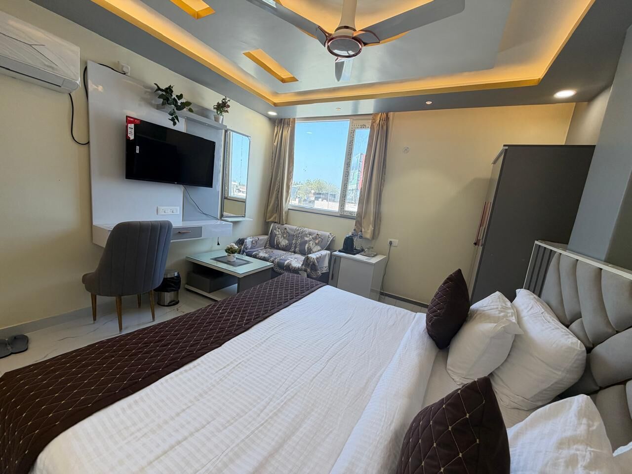 A hotel room with a bed, a desk, a chair, a TV, and a ceiling fan.