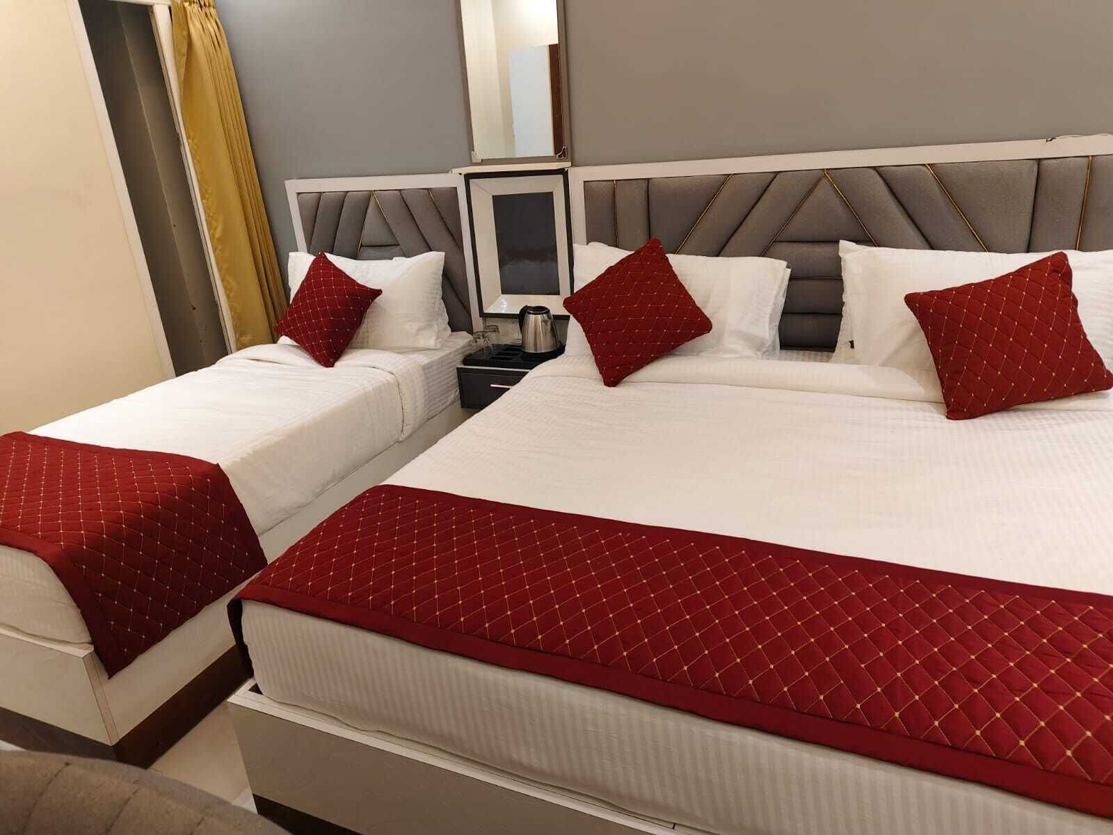 Deux lits avec du linge de lit blanc et des oreillers rouges, une table de chevet avec une lampe et un miroir au mur.