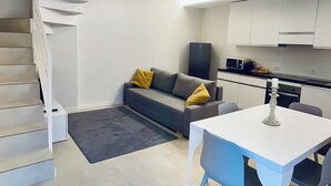 A modern living space with a staircase, a grey sofa with yellow cushions, a dining table with chairs, and a kitchen area with cabinets and appliances. - Sweet & Home 1 LOFT on two levels near bergamo (Azzano San Paolo)