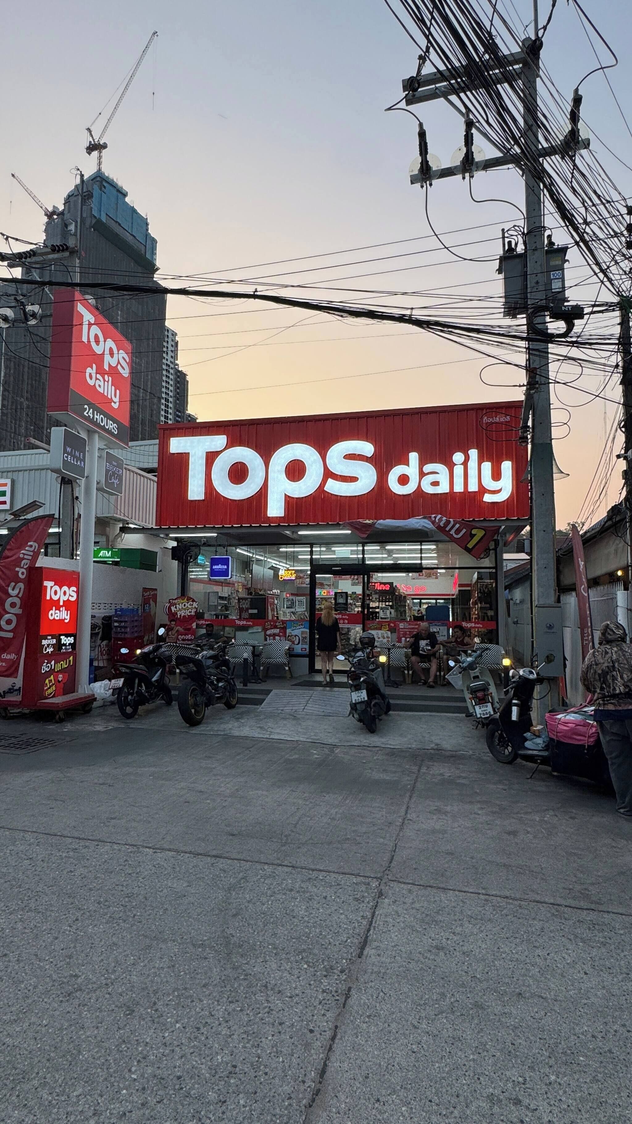 A Tops Daily store with a prominent red sign, motorcycles parked in front, and a clear sky.