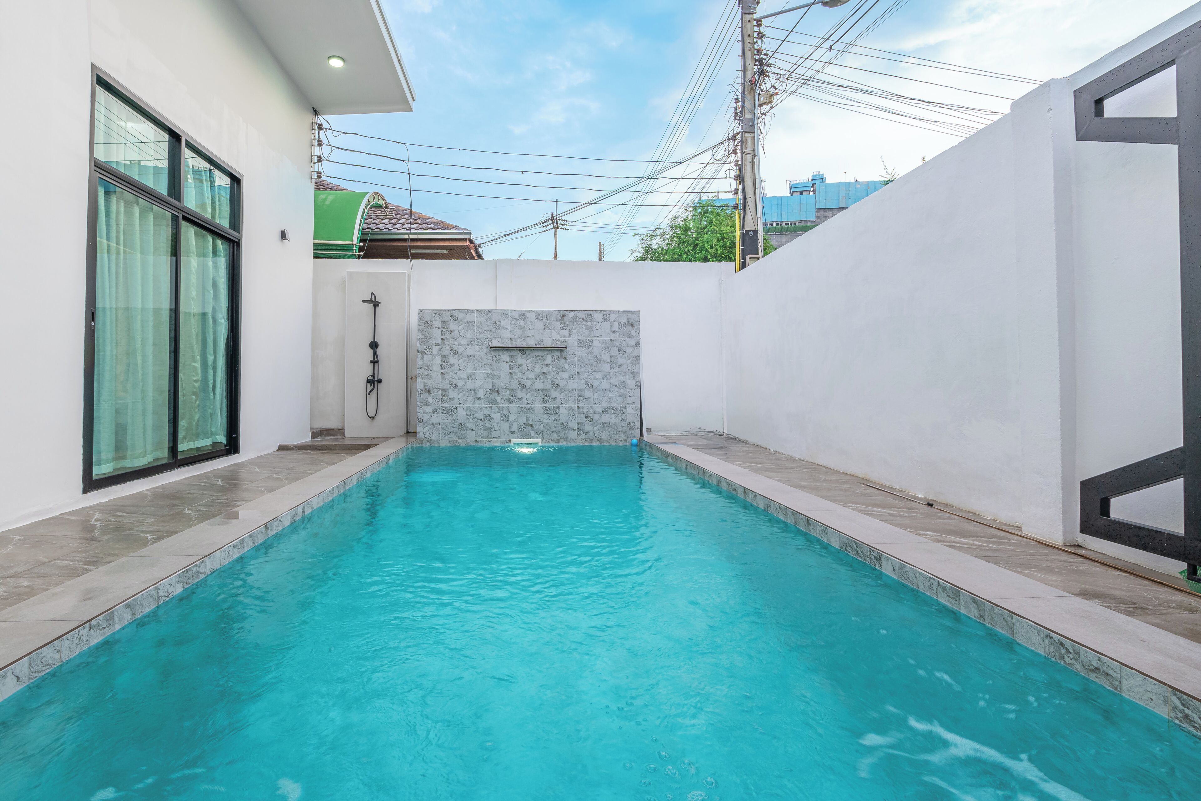 Una piscina con bordo piastrellato, una porta in vetro e un muro bianco dalla texture simile al marmo.