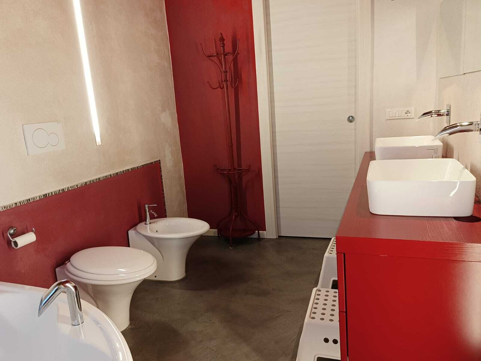 Ett badrum med ett vitt handfat, toalett och bidé, ett rött sminkbord och en spegel.