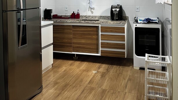A modern kitchen with white tiles, a stainless steel refrigerator, wooden cabinets, a built-in oven, and a coffee maker. - Apartment on Dunas beach, 6 minutes from Forte beach in Cabo Frio. (Cabo Frio)