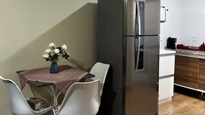 A compact kitchen with a refrigerator, microwave, and wooden cabinets. There is a dining table with a vase of flowers and two chairs. - Apartment on Dunas beach, 6 minutes from Forte beach in Cabo Frio. (Cabo Frio)