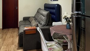 A compact living space with a sofa, a dining table with chairs, a refrigerator, a ceiling fan, and a door. - Apartment on Dunas beach, 6 minutes from Forte beach in Cabo Frio. (Cabo Frio)
