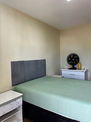 A bedroom with a bed, a nightstand, a dresser, and a wall-mounted fan. - Apartment on Dunas Beach, 6 minutes from Forte Beach in Cabo Frio. (Cabo Frio)