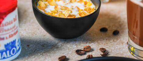 Un tazón de cereal con leche, un vaso de jugo de naranja y un envase de leche.