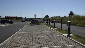 A paved walkway with a fence, street lamps, and parked cars.