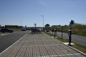 A paved walkway with a fence, street lamps, and parked cars.