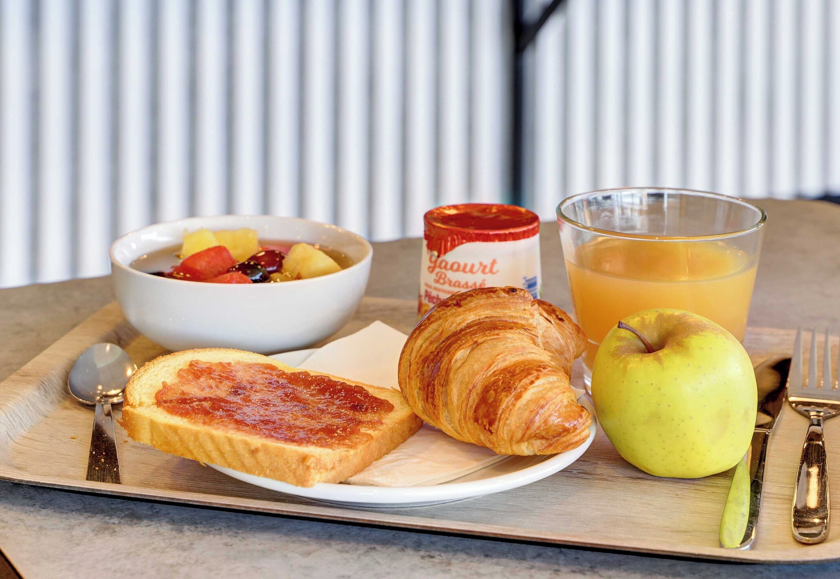 Bandeja de desayuno con tostadas, un croissant, un tazón de fruta, un vaso de jugo de naranja y un frasco de mermelada.