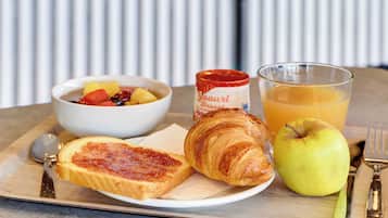 Bandeja de desayuno con tostadas, un croissant, un tazón de fruta, un vaso de jugo de naranja y un frasco de mermelada.