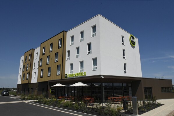 A multi-story hotel with a modern design, outdoor seating area, and a visible restaurant sign.