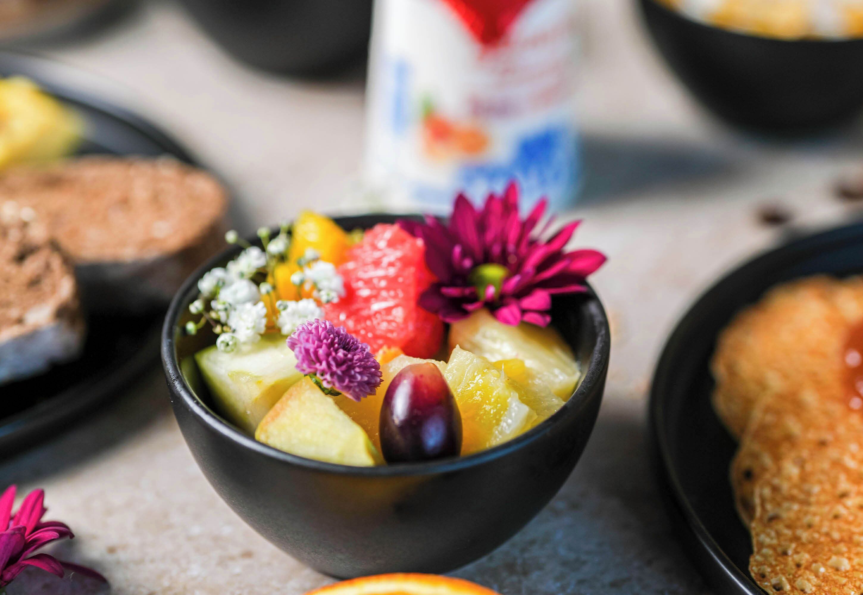 A bowl of fruit salad with various fruits and flowers.