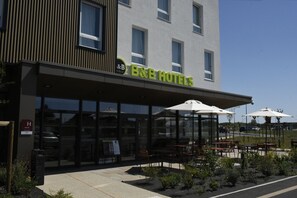 A B&B hotel with a modern facade, outdoor seating, and a clear view of the street.