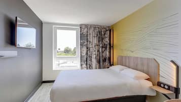 Ein Hotelzimmer mit Bett, Wandfernseher, Fenster mit Vorhängen und einem Wandbild.