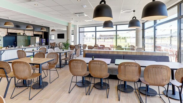 A modern restaurant with high tables, chairs, and pendant lighting.