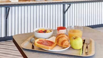 Un safata de petitdejuni amb torrades, un croissant, una poma, un got de suc d'aranja i un bol de fruita damunt d'una taula.