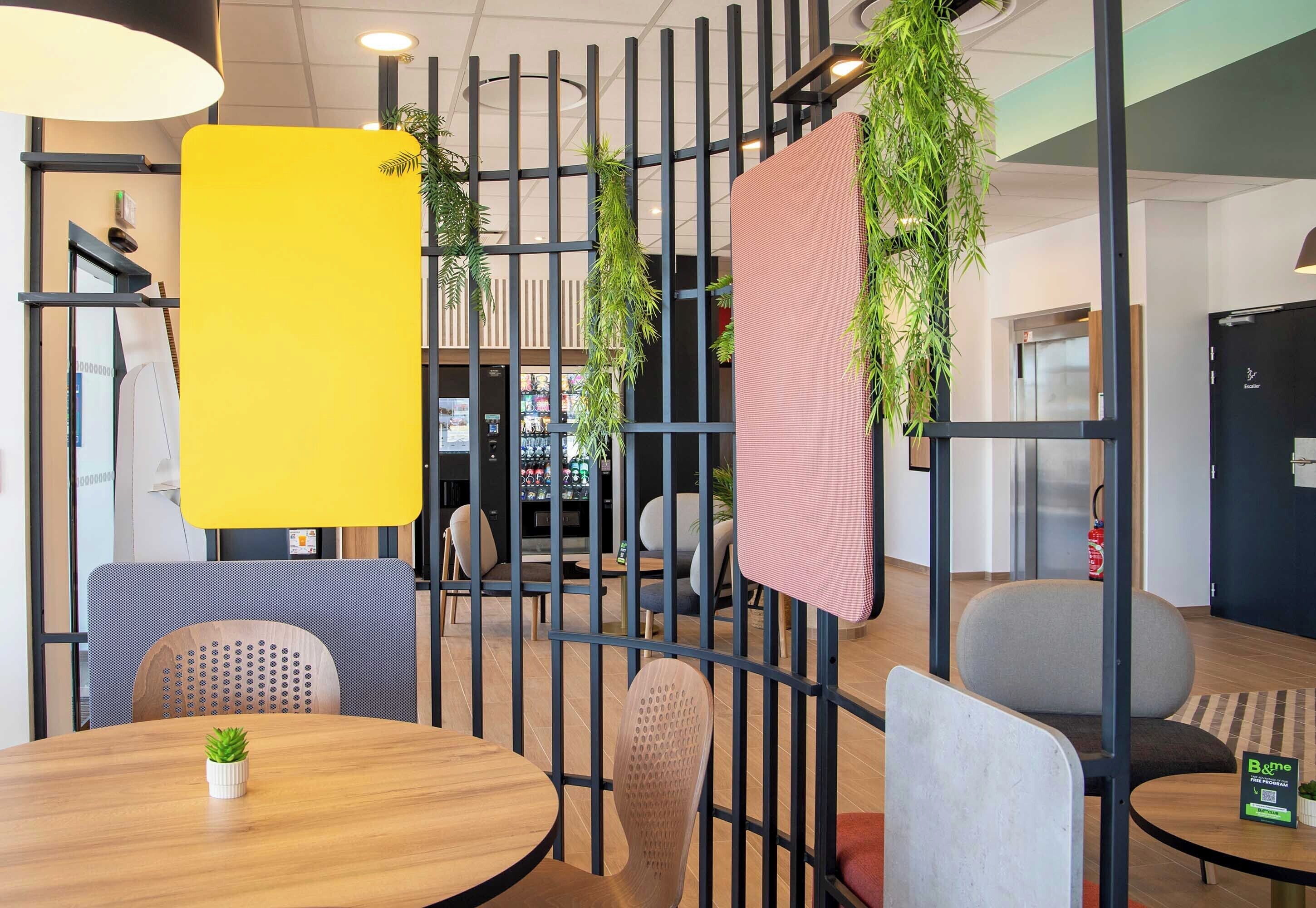 Un interior moderno con una mesa de madera, sillas, un separador amarillo y plantas colgantes.