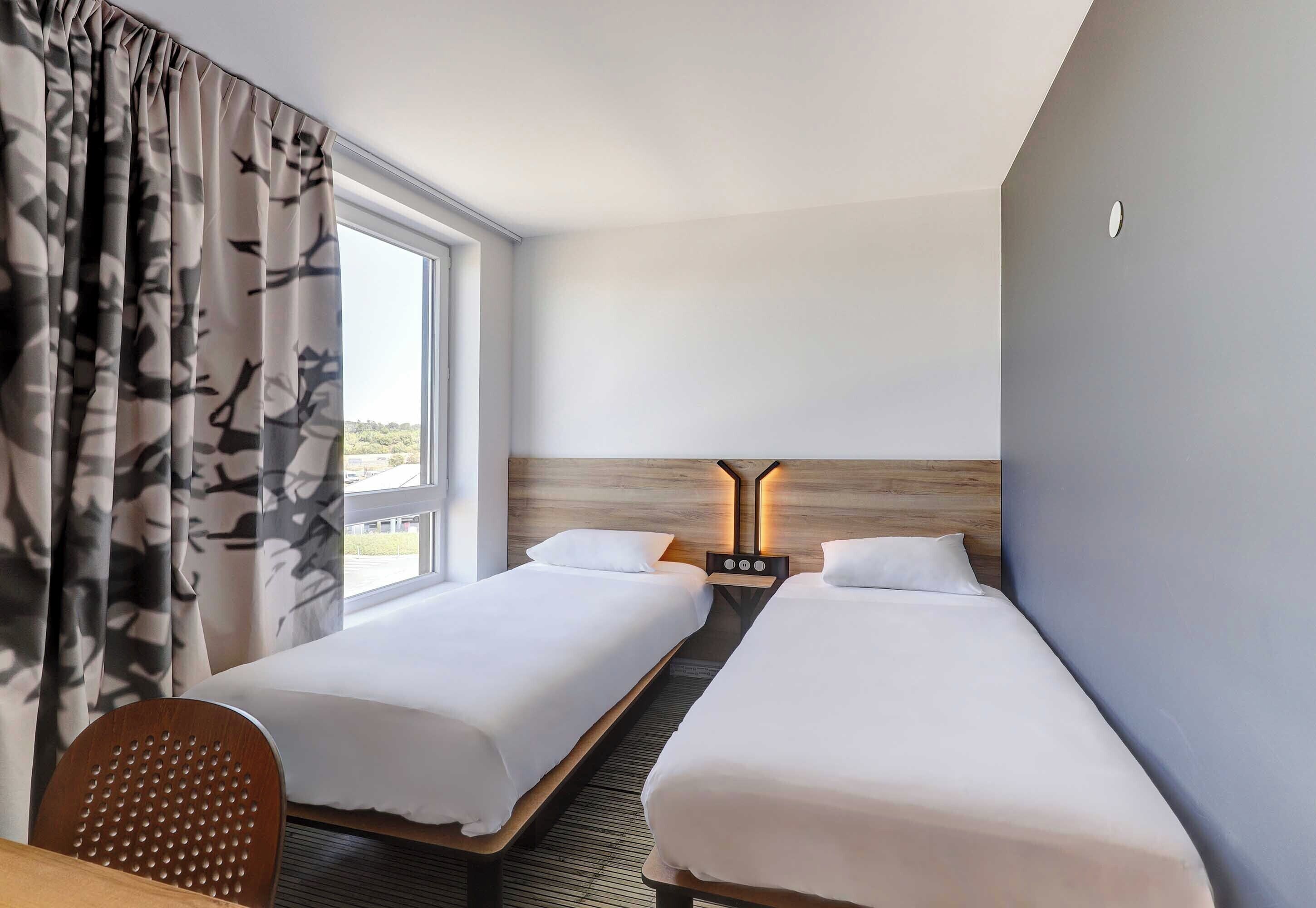 A hotel room with two beds, a wooden headboard, a desk, and a chair.