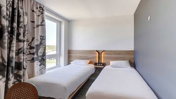 A hotel room with two beds, a wooden headboard, a desk, and a chair.