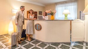 A hotel reception area with a check-in counter, a reception desk, a large window with curtains, and a lamp. - Charming and Comfy Apartment in Alghero (Alghero)
