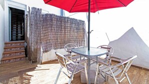 Een terras met een ronde tafel en stoelen, een rode parasol en uitzicht op een gebouw met trappen en een houten omheining.