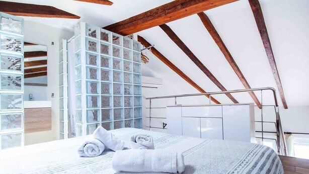 Een slaapkamer met een schuine kap, een bed met opgerolde handdoeken, een kledingkast en een glazen displaykast.
