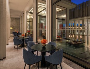 Un moderno vestíbulo de hotel con piscina protegida por vidrio, suelo de mármol y mobiliario contemporáneo.