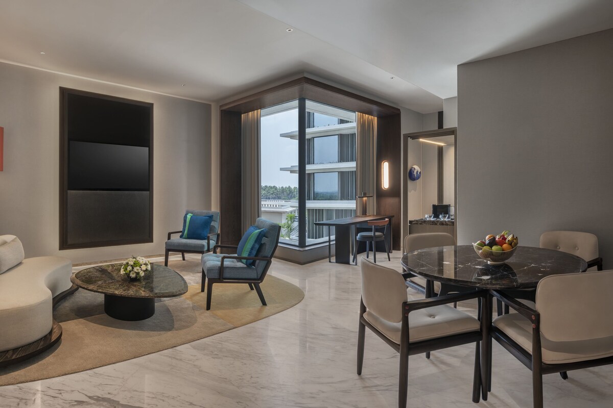 A modern living room with a sofa, chairs, a coffee table, a dining table, and a large window with a view.