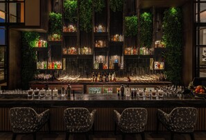 A bar area with multiple shelves of liquor bottles, a bar counter with glasses, and three patterned chairs. - The Residency Signature Madurai (Madurai)