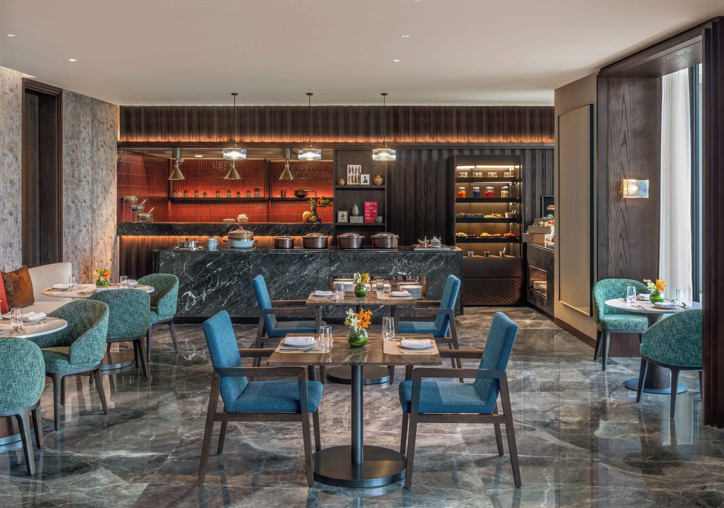 Un espace repas moderne avec un sol en marbre, des chaises recouvertes d’un tissu bleu et un îlot central doté d’un bar.