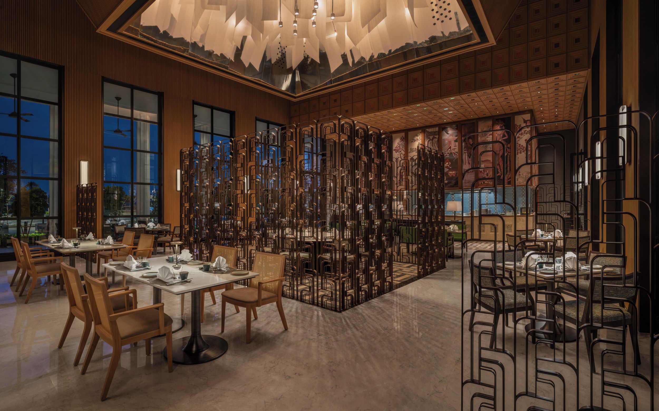 A modern restaurant interior with high ceilings, wooden paneling, and a central decorative wall.