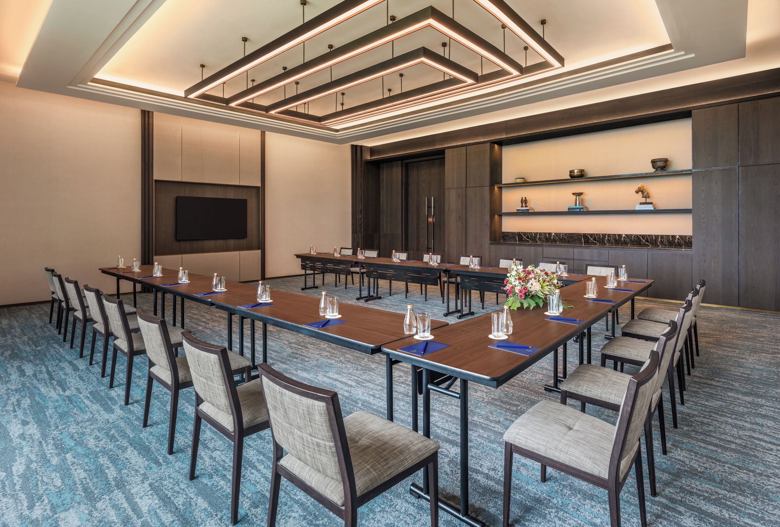 A conference room with a long table, chairs, a flat-screen TV, and a decorative shelf with items.