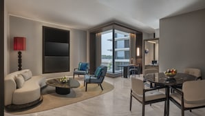A modern living room with a sofa, chairs, a coffee table, a dining table, and a large window with a view. - The Residency Signature Madurai (Madurai)