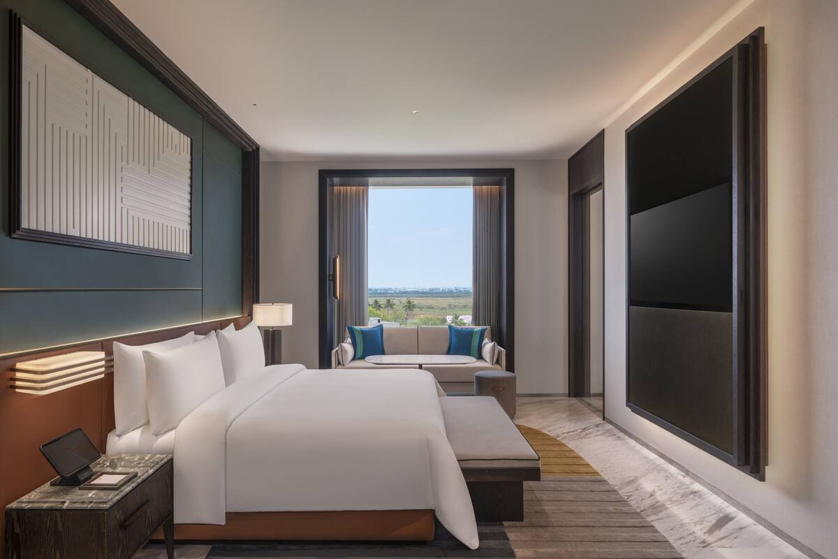 A hotel room with a large bed, a sofa, a TV, and a view of the outdoors.