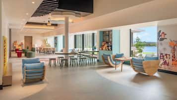 A spacious indoor area with multiple seating arrangements, including chairs and tables, and a large window providing a view of the outdoors.
