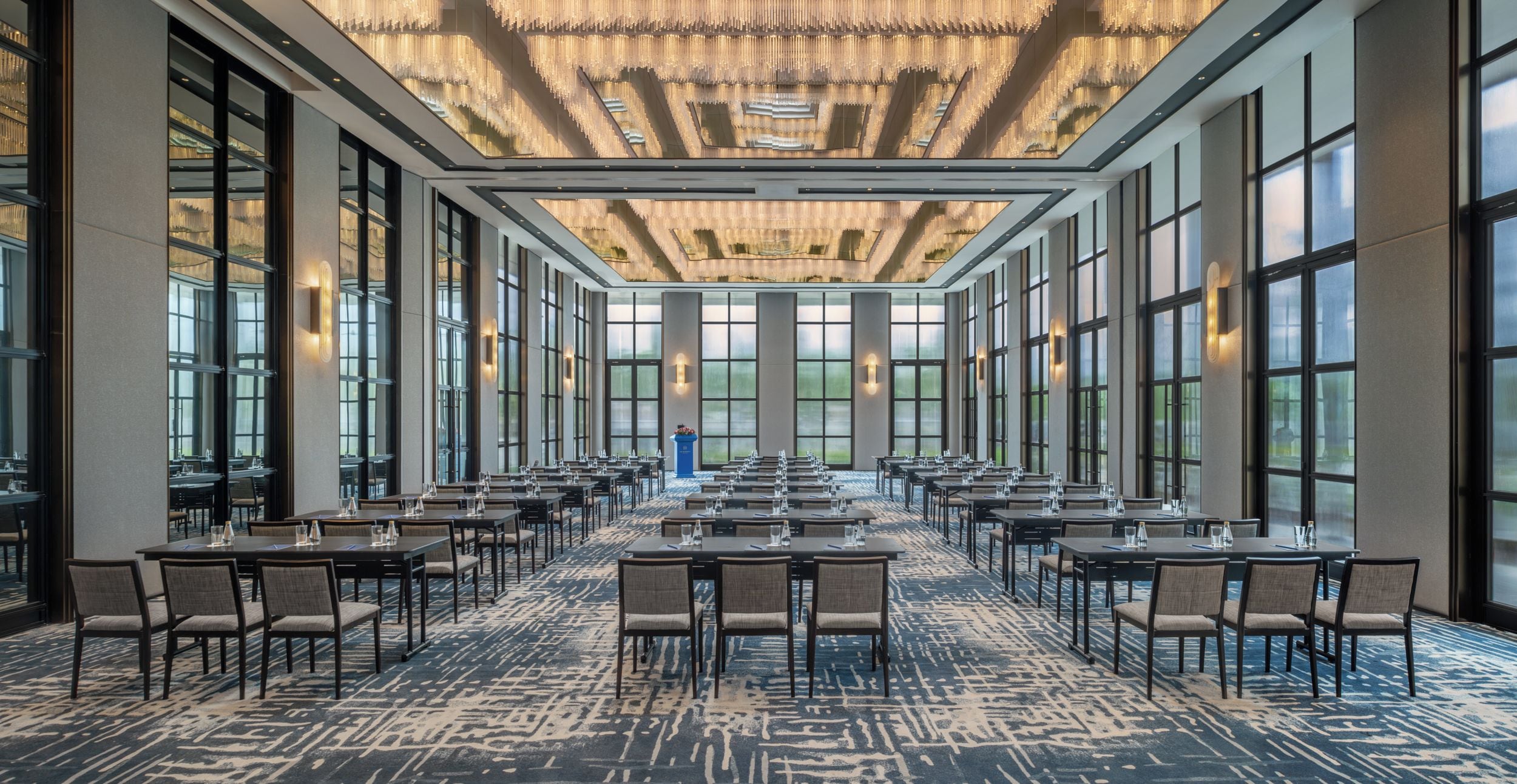 A conference room with a long table and chairs, large windows, and a patterned carpet.