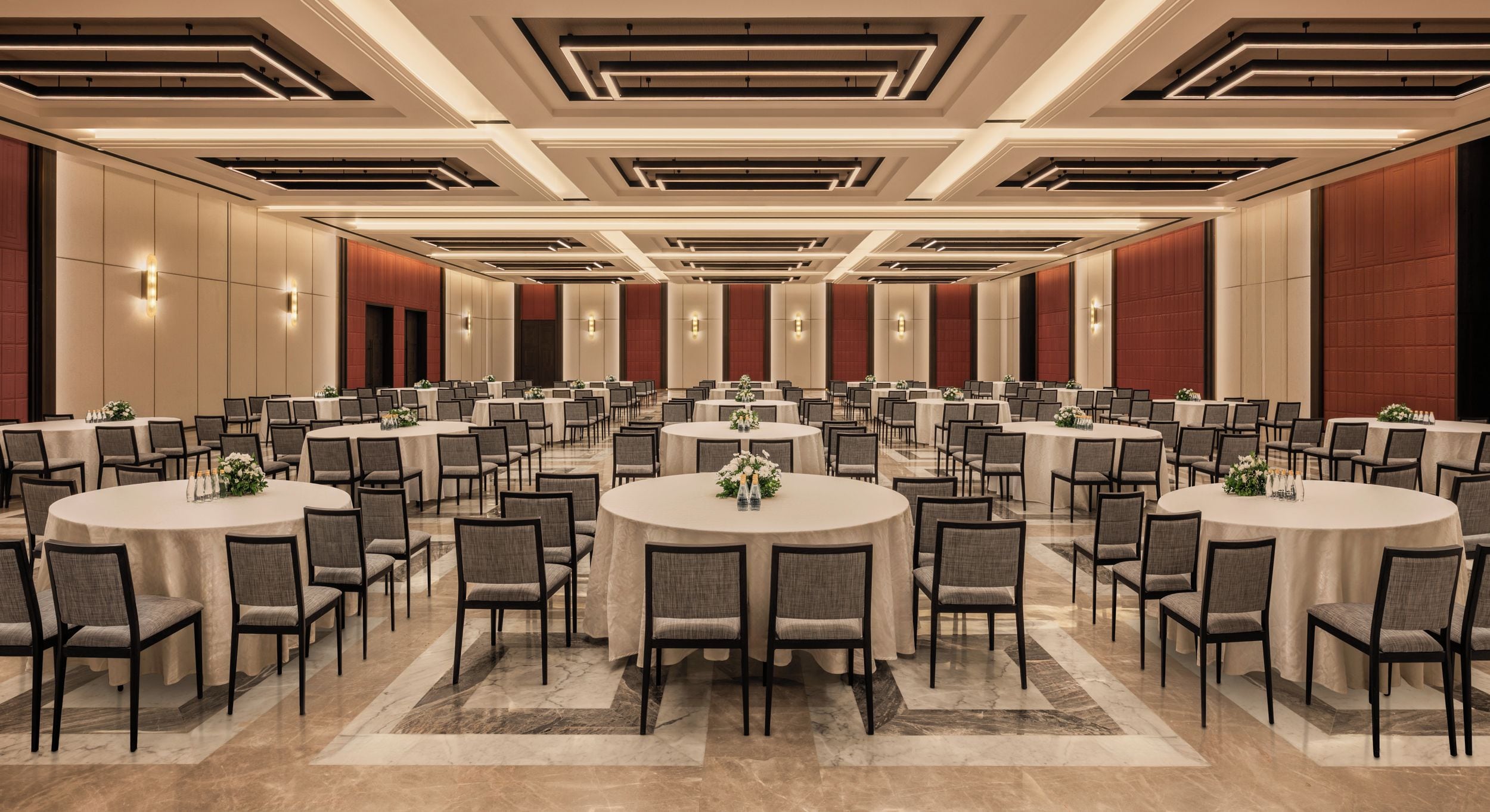 A large conference room with multiple round tables and chairs, arranged in rows.