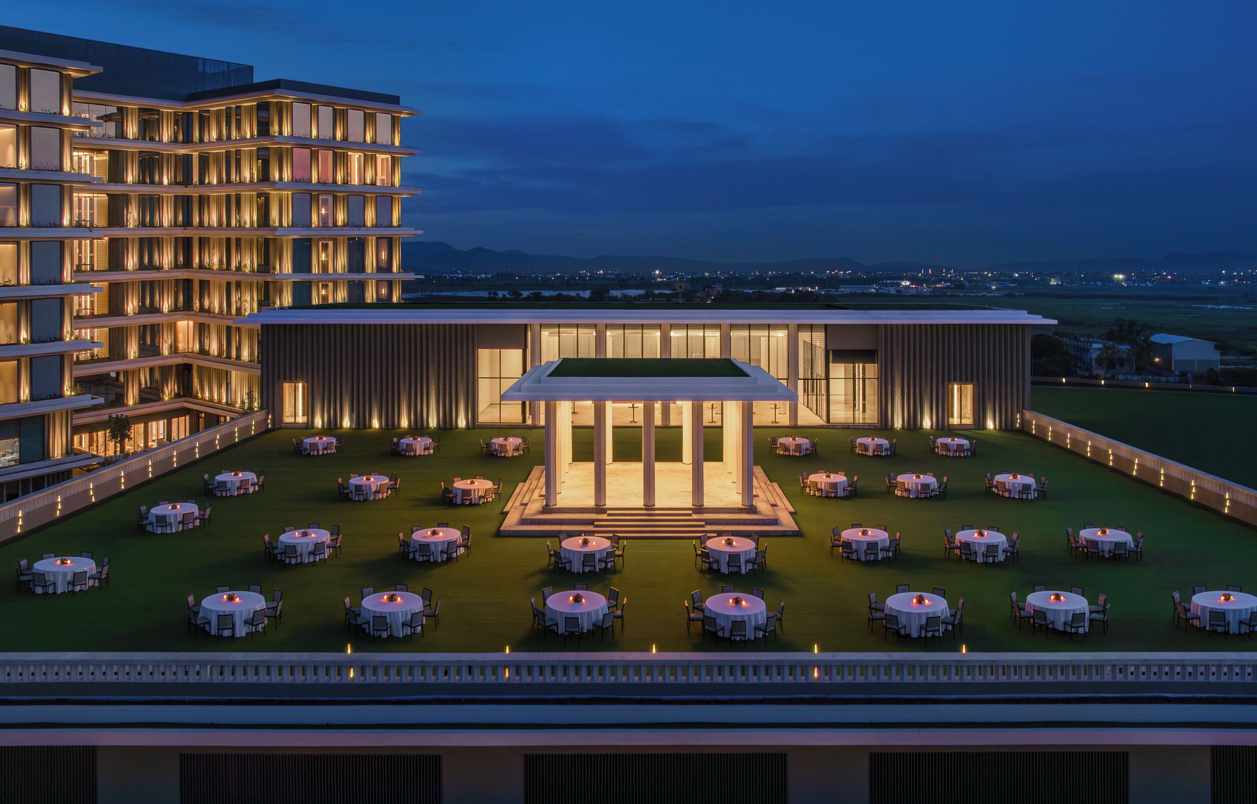 A multi-story hotel with a rooftop dining area featuring round tables and chairs.