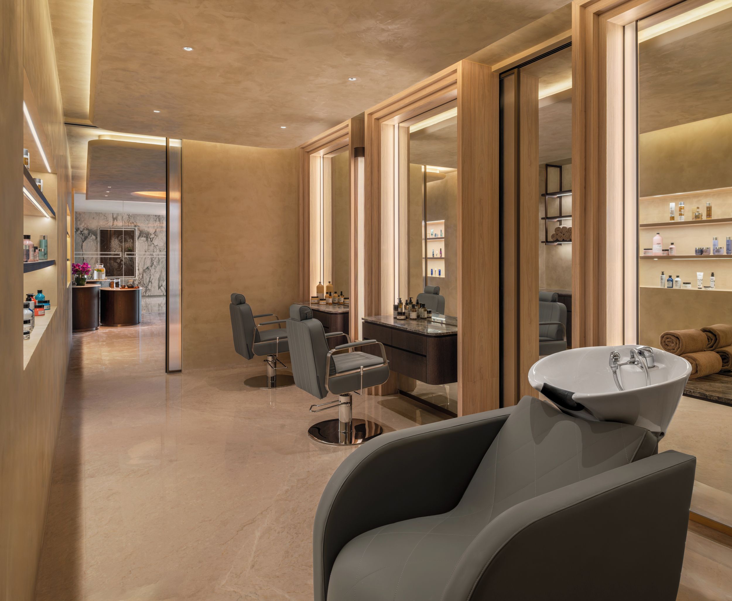A modern hair salon interior with a central seating area, a large mirror, and shelves with hair products.