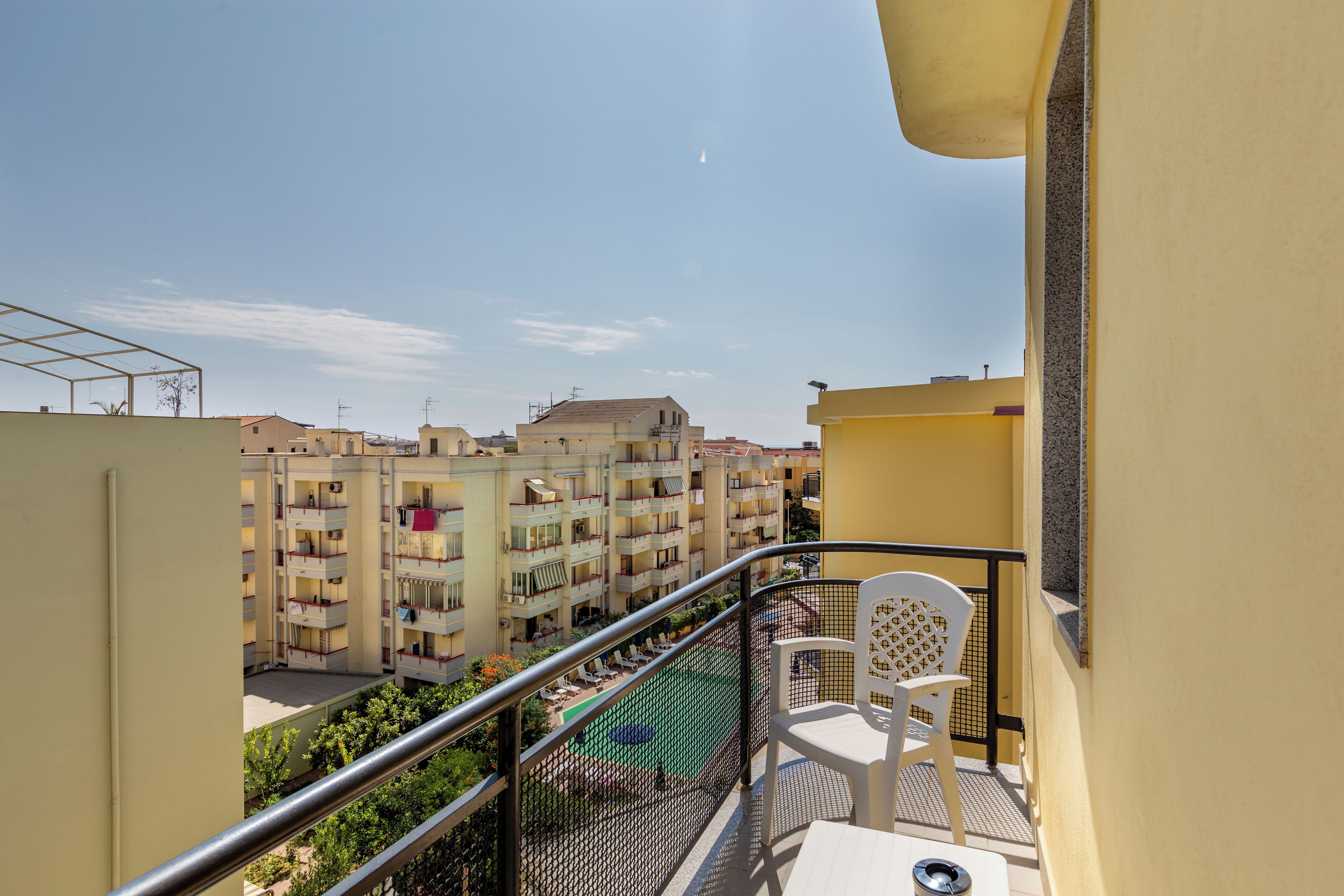 Ein Balkon mit Blick auf einen Wohnkomplex, einen Pool und einen Stuhl.