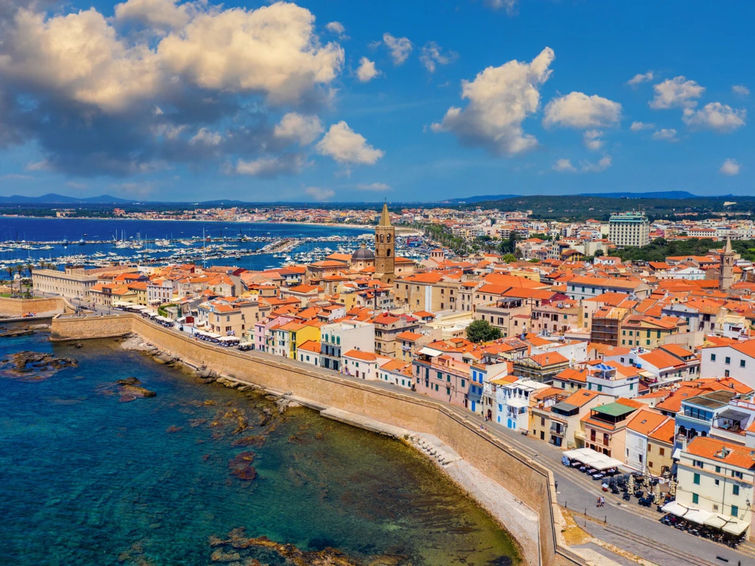 A coastal cityscape with historic buildings, a prominent tower, and a marina.