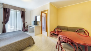 Ett hotellrum med en säng, ett skrivbord, en dator, en soffa och ett matbord med stolar.