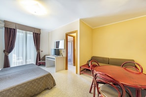 Ein Hotelzimmer mit Bett, Schreibtisch, Computer, Sofa und Esstisch mit Stühlen.