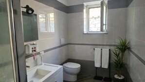 Moderni kylpyhuone, jossa on valkoinen pesuallas, wc ja pieni ikkuna.