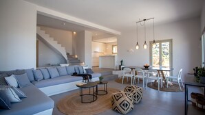 Een moderne woonkamer met een bank, salontafel, poefs en een eethoek met stoelen en een tafel.