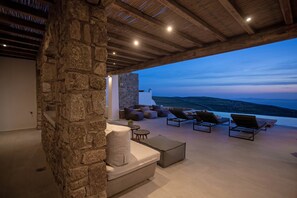 A stone wall and wooden ceiling in a room with a view of the sea. - Villa Chimera with private pool - My Rental Homes (Mykonos)