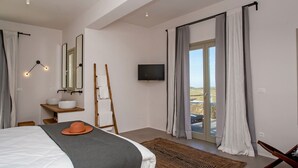 Een moderne slaapkamer met een bed, een televisie, een badkamer met een wastafel en spiegel, en uitzicht op de omgeving.