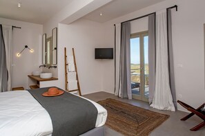 A modern bedroom with a bed, a TV, a bathroom with a sink and mirror, and a view of the outdoors. - Villa Chimera with private pool - My Rental Homes (Mykonos)